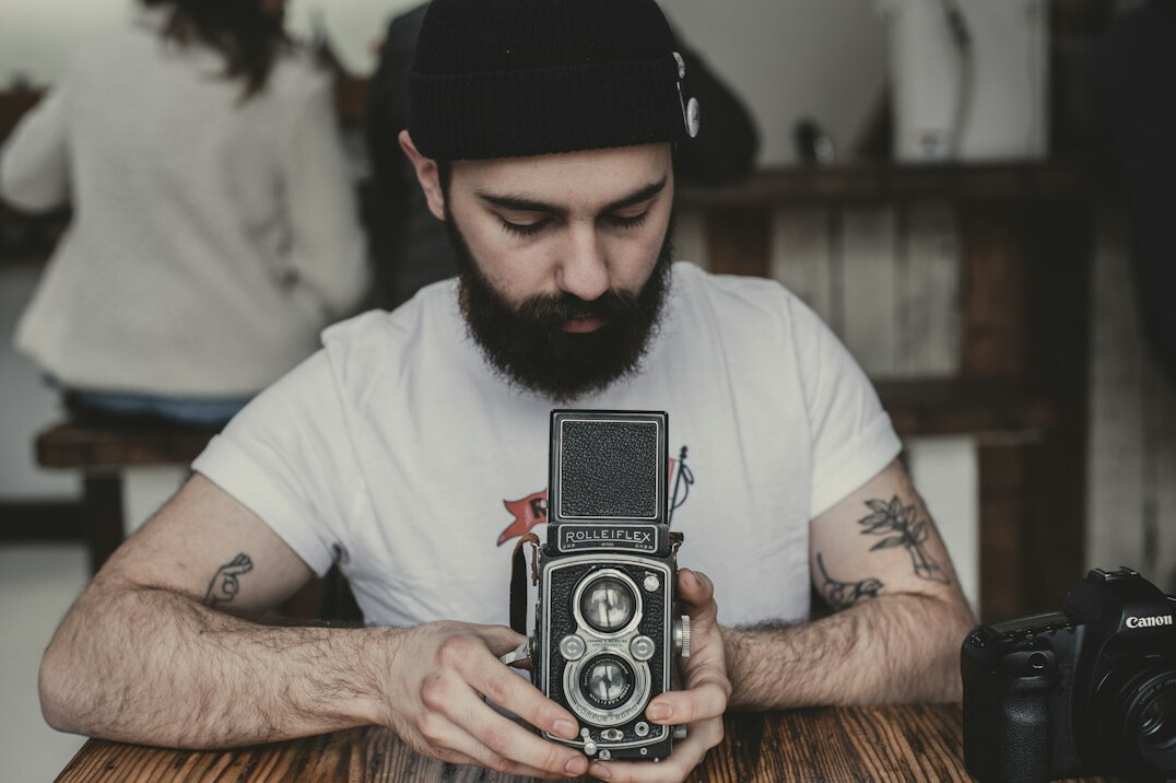 Studio portrait of a Danish man documentary photographer in his forties with a beard and a camera around his neck